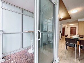 Ein modernes Interieur mit Glastür zum Balkon, einem Essbereich mit Tisch und Stühlen sowie einer im Hintergrund sichtbaren Küche.
