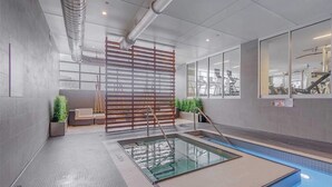 Ein moderner, überdachter Poolbereich mit einem gläsernen Anbau, einer Holzlamellen-Abteilung und Trainingsgeräten im Hintergrund.