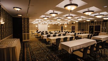 Un salón de banquetes con varias mesas y sillas, un escenario y papel tapiz estampado.