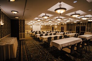 Un salón de banquetes con varias mesas y sillas, un escenario y papel tapiz estampado.