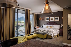 Habitación de hotel con una cama grande, un escritorio, una silla, una ventana con cortinas y vistas a una montaña.