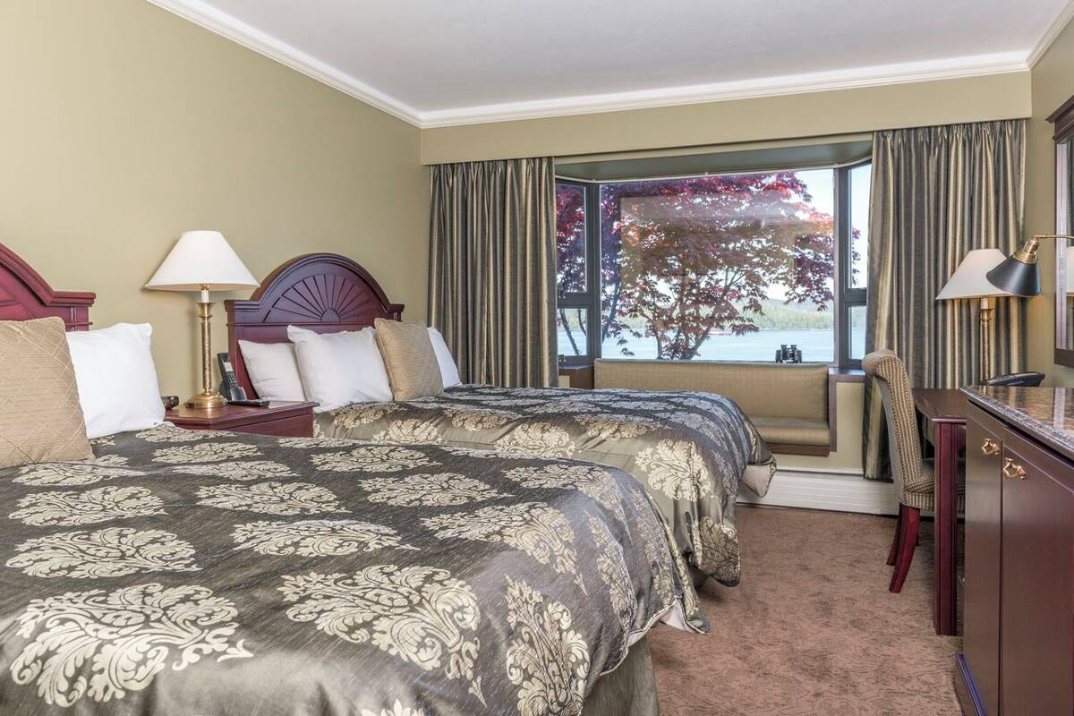 Une chambre d’hôtel avec un grand lit, deux tables de chevet, un bureau et une vue sur un lac.