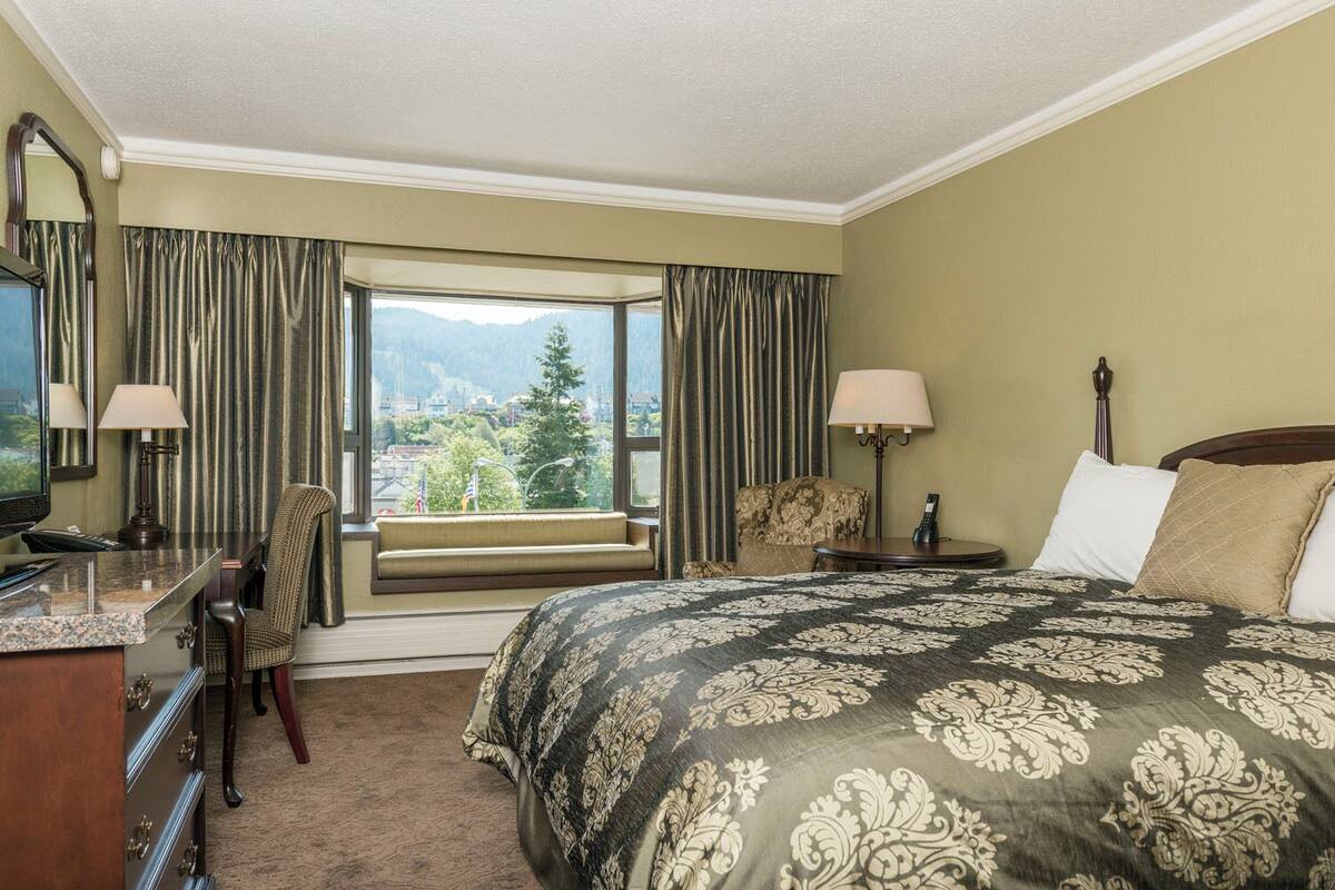 Une chambre d’hôtel avec un grand lit, un bureau avec une chaise, une lampe et une vue sur une montagne par la fenêtre.