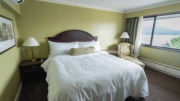 A hotel room with a large bed, two bedside lamps, a chair, and a window with a view.