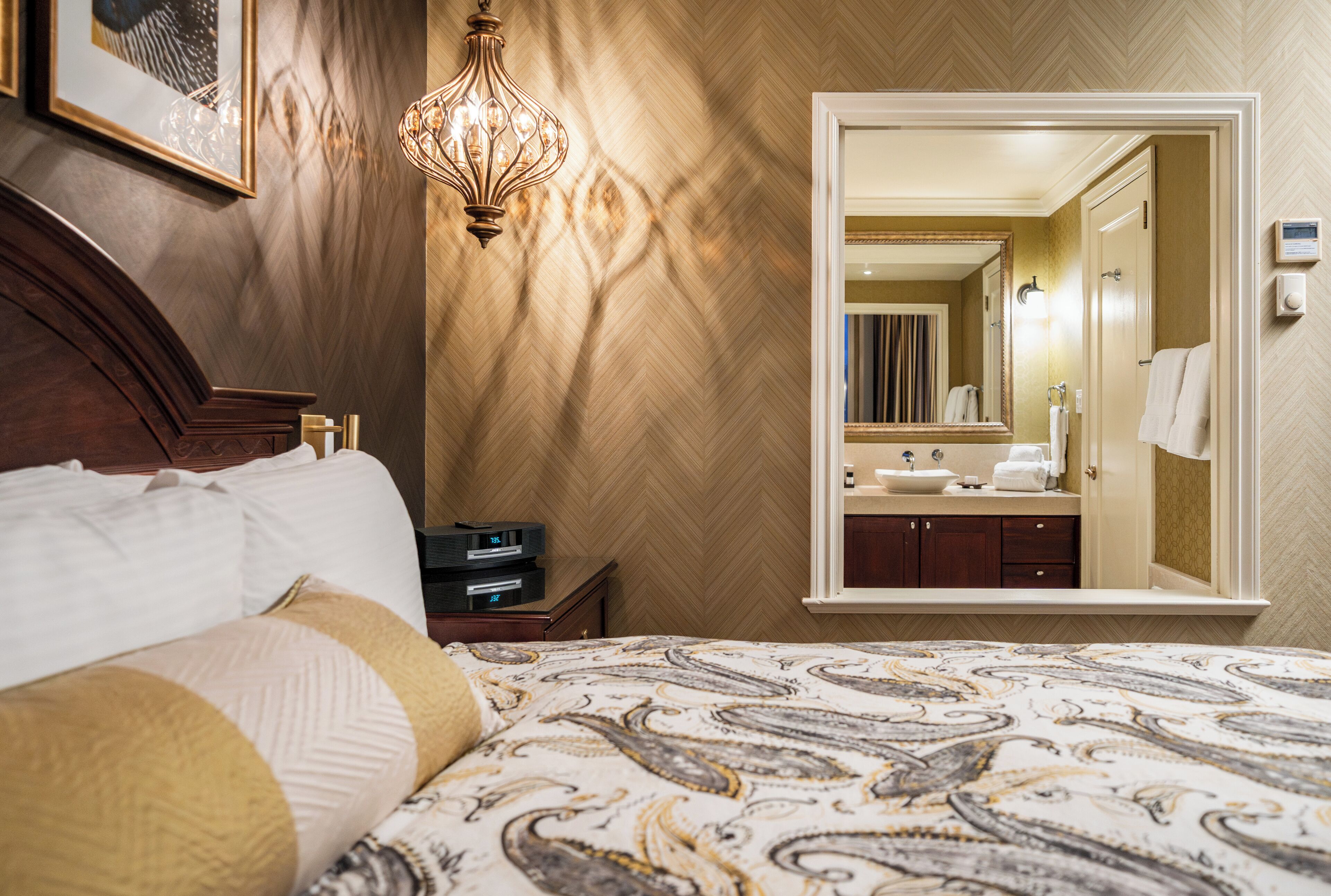 Een hotelkamer met een bed, een nachtkastje met een lamp, een grote spiegel en een badkamer die door een geopende deur zichtbaar is.