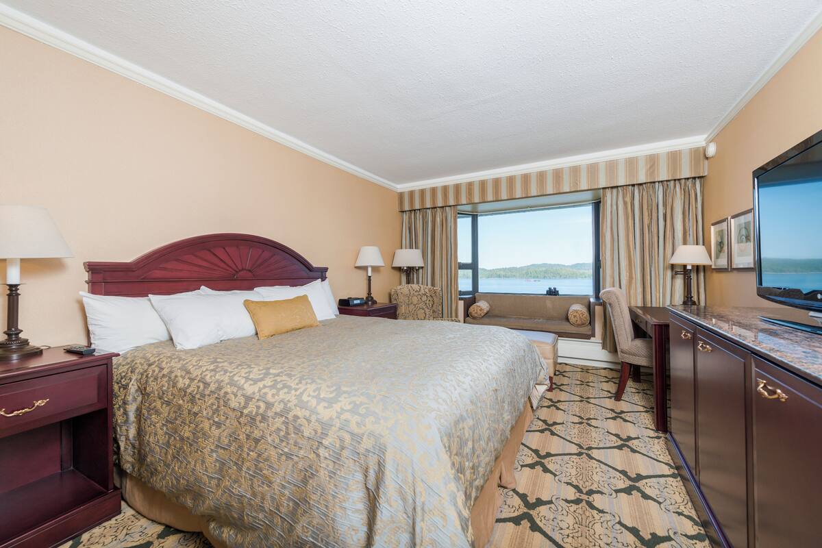 Une chambre d’hôtel avec un grand lit, deux tables de chevet, un bureau avec une chaise, une télévision et une fenêtre avec des rideaux.