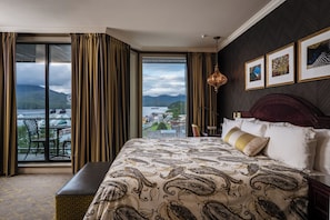 Une chambre dâhĂŽtel dotĂ©e dâun grand lit, offrant une vue sur un lac et des montagnes, dâun coin repas avec une table et des chaises, et dâun lustre.