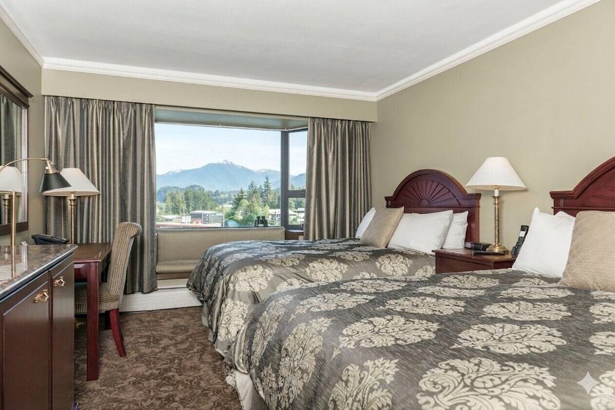 Une chambre d’hôtel avec un grand lit, deux tables de chevet, un bureau avec une chaise et une vue sur les montagnes par une grande fenêtre.