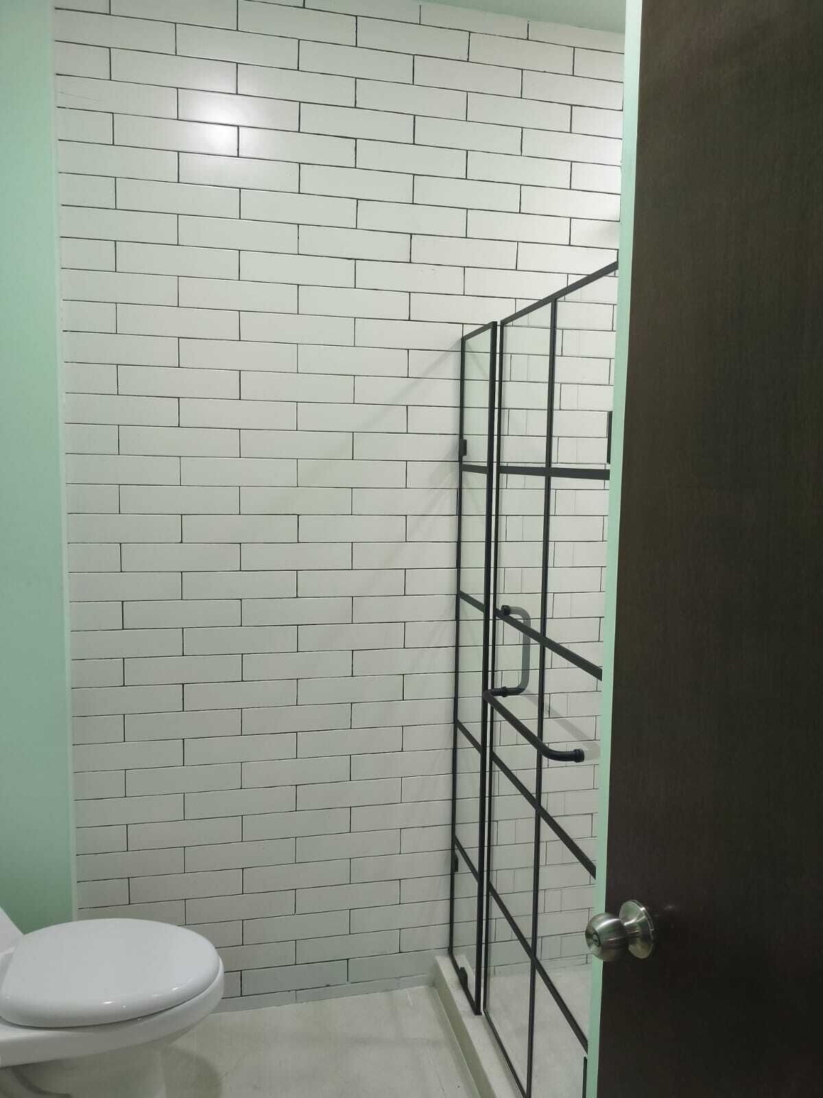 Un baño con paredes de azulejos blancos, un inodoro blanco y una puerta con manija de metal.