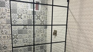 Un baño con baldosas estampadas, cabina de ducha con mampara de cristal, inodoro blanco y lavamanos con espejo.
