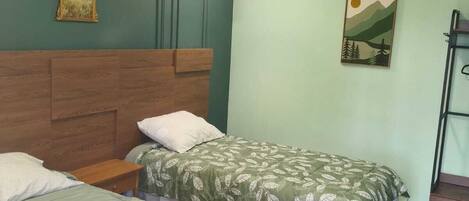 A room with two beds, a wooden headboard, a wall-mounted air conditioner, and a painting.