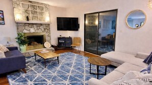 A living room with a stone fireplace, a flat-screen TV, a sofa, a coffee table, and a patterned rug. - Peaceful 3BR w Hot Tub, in Rumbling Bald, Lake Lure, Resort amenities included (Lake Lure)