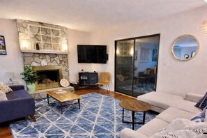 Ein Wohnzimmer mit Kamin aus Stein, einem Flachbildfernseher, einer Couch, einem Couchtisch und einem gemusterten Teppich.