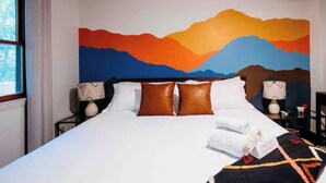 A hotel room with a large bed, a painting of mountains on the wall, and a window with curtains. - Peaceful 3BR w Hot Tub, in Rumbling Bald, Lake Lure, Resort amenities included (Lake Lure)