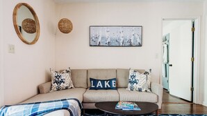 A living room with a sofa, a coffee table, a patterned rug, a wall-mounted mirror, and a painting. - Peaceful 3BR w Hot Tub, in Rumbling Bald, Lake Lure, Resort amenities included (Lake Lure)