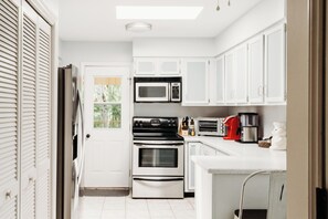 Eine Küche mit weißen Schränken, einer Mikrowelle, einem Backofen und einer Kaffeemaschine.