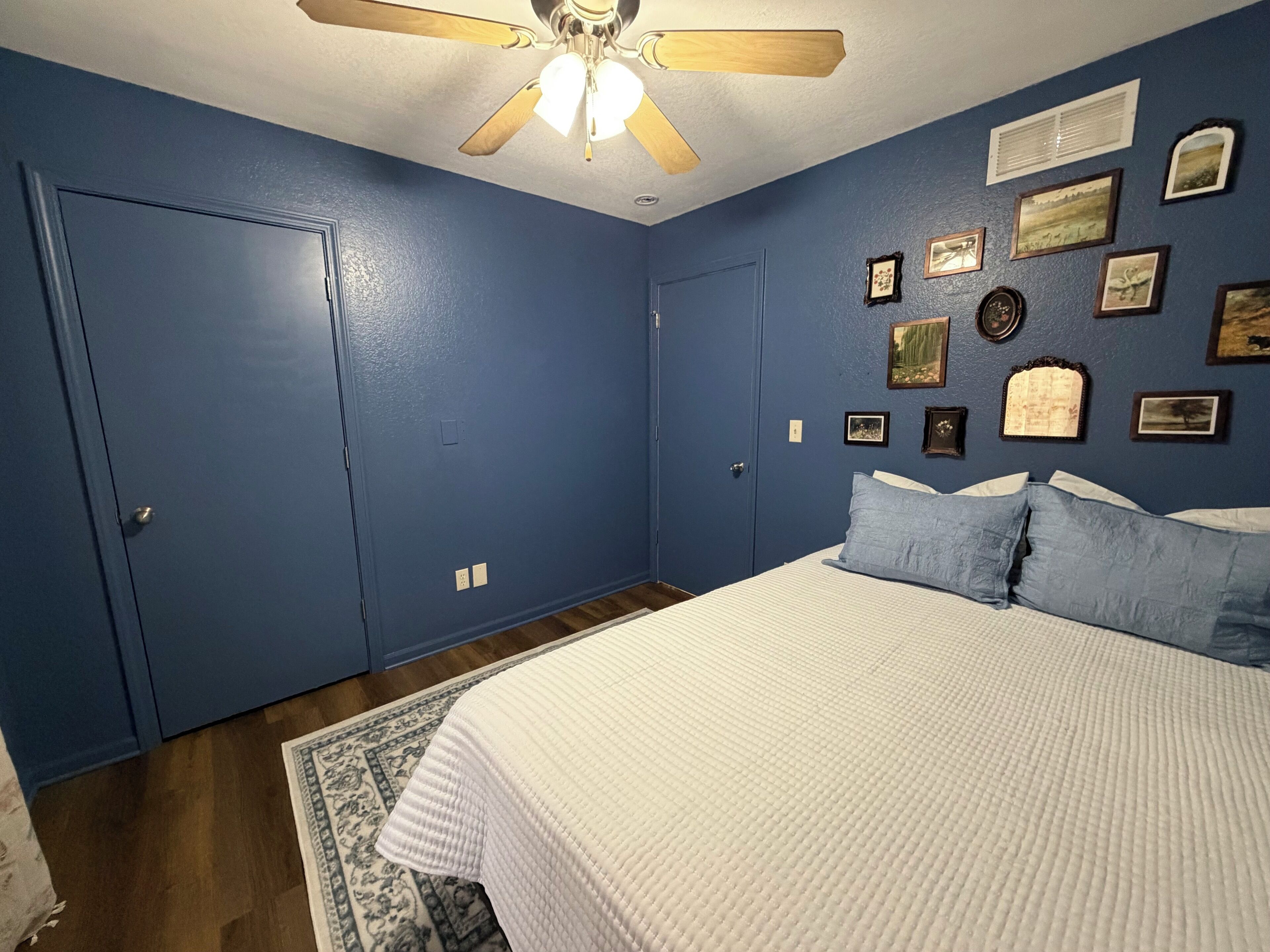A bedroom with a bed, a ceiling fan, and wall-mounted pictures.