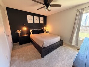 Ein Schlafzimmer mit einem Bett, Nachttischen, einem Deckenventilator und einem Fenster mit Vorhängen.
