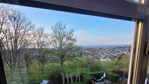 Blick durch ein Fenster in einen Garten mit Rasen, einem runden Gartenornament und einem Holzzaun.