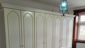 Ein Schlafzimmer mit großem Kleiderschrank, einem Bett mit weißer Daunendecke und einem Fenster mit Jalousien.