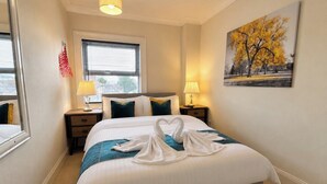 Ein Hotelzimmer mit einem großen Bett, zwei Nachttischen, einem Fenster mit Jalousien, einem Bild an der Wand und einer Deckenleuchte.