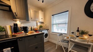 Eine moderne Küche mit Backofen, ein Essbereich mit Tisch für zwei Personen und ein Fenster mit Jalousien.