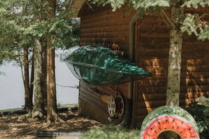A wooden cabin with a large glass greenhouse structure, a wooden door, and a tree in the foreground.