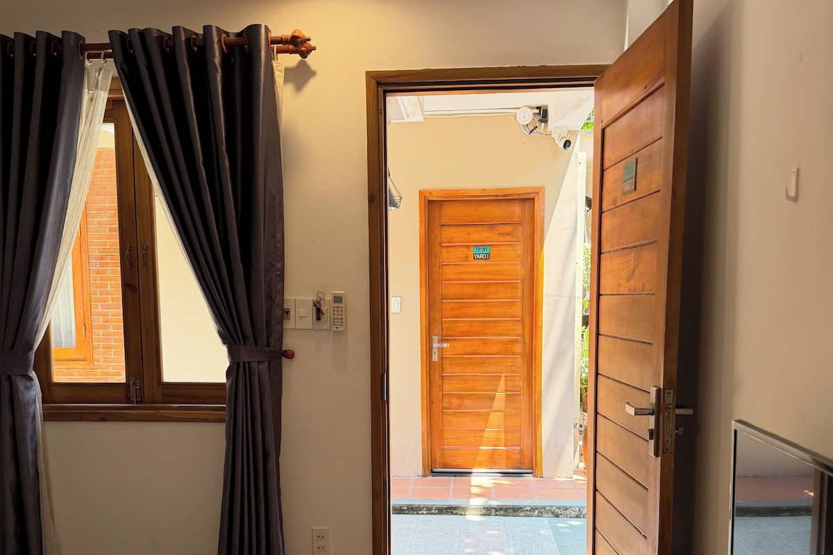 Una habitación de hotel con cama, televisión, puerta de madera que da al exterior y ventana con cortinas.