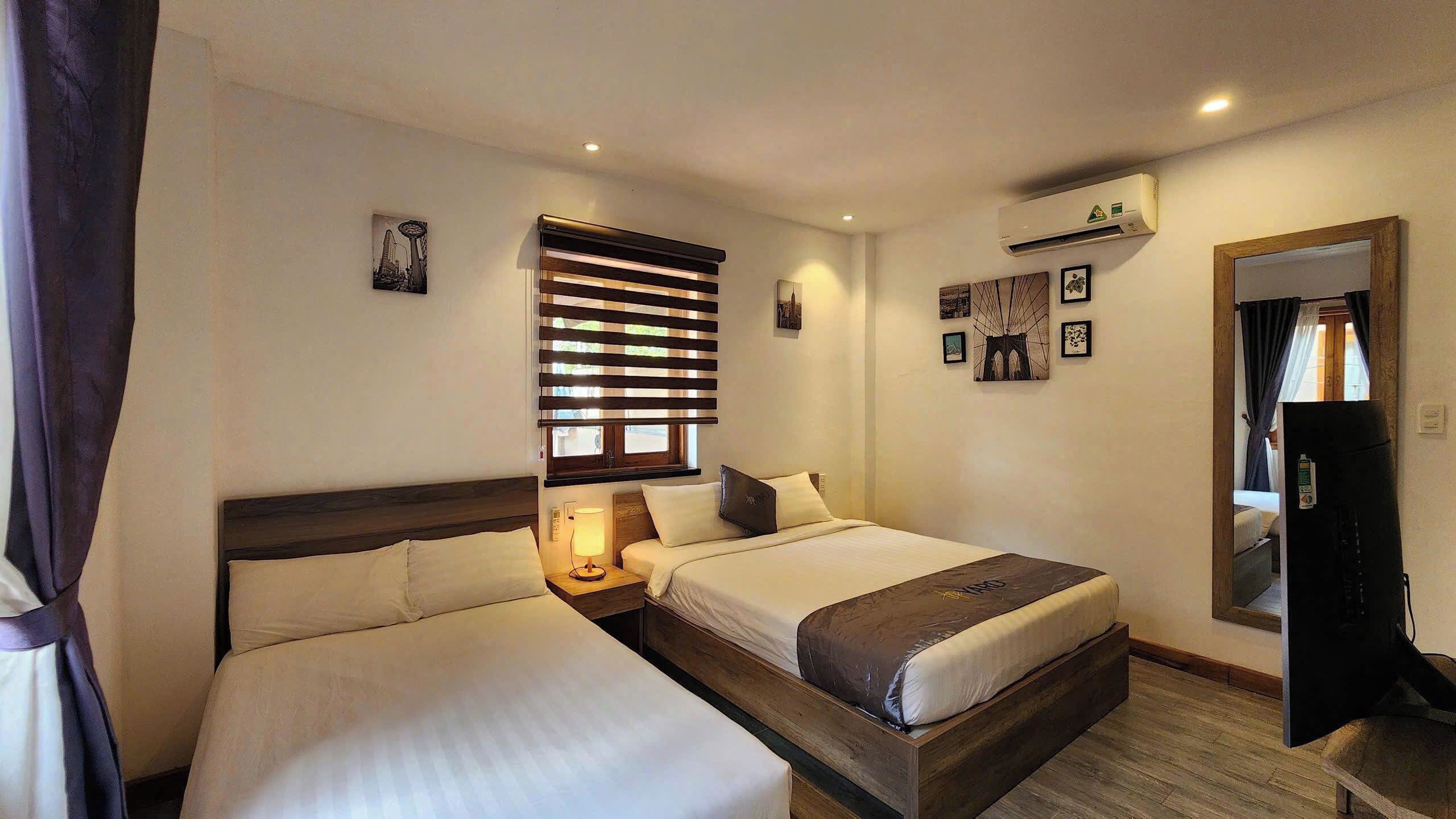 Habitación de hotel con dos camas, una ventana con persianas, un aire acondicionado instalado en la pared y un espejo.