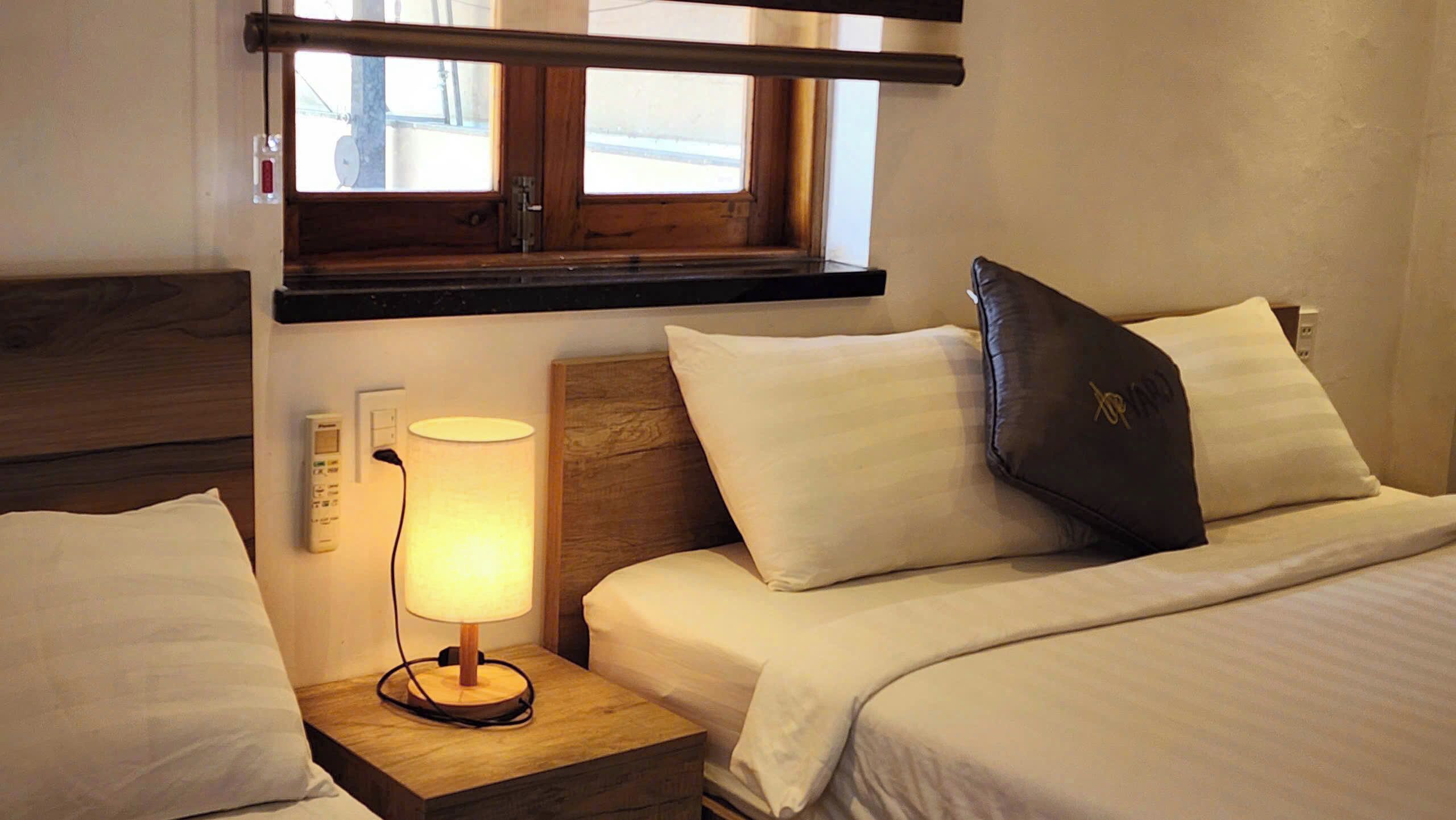 A hotel room with a wooden headboard, a bedside lamp, a nightstand, and a window with a view.