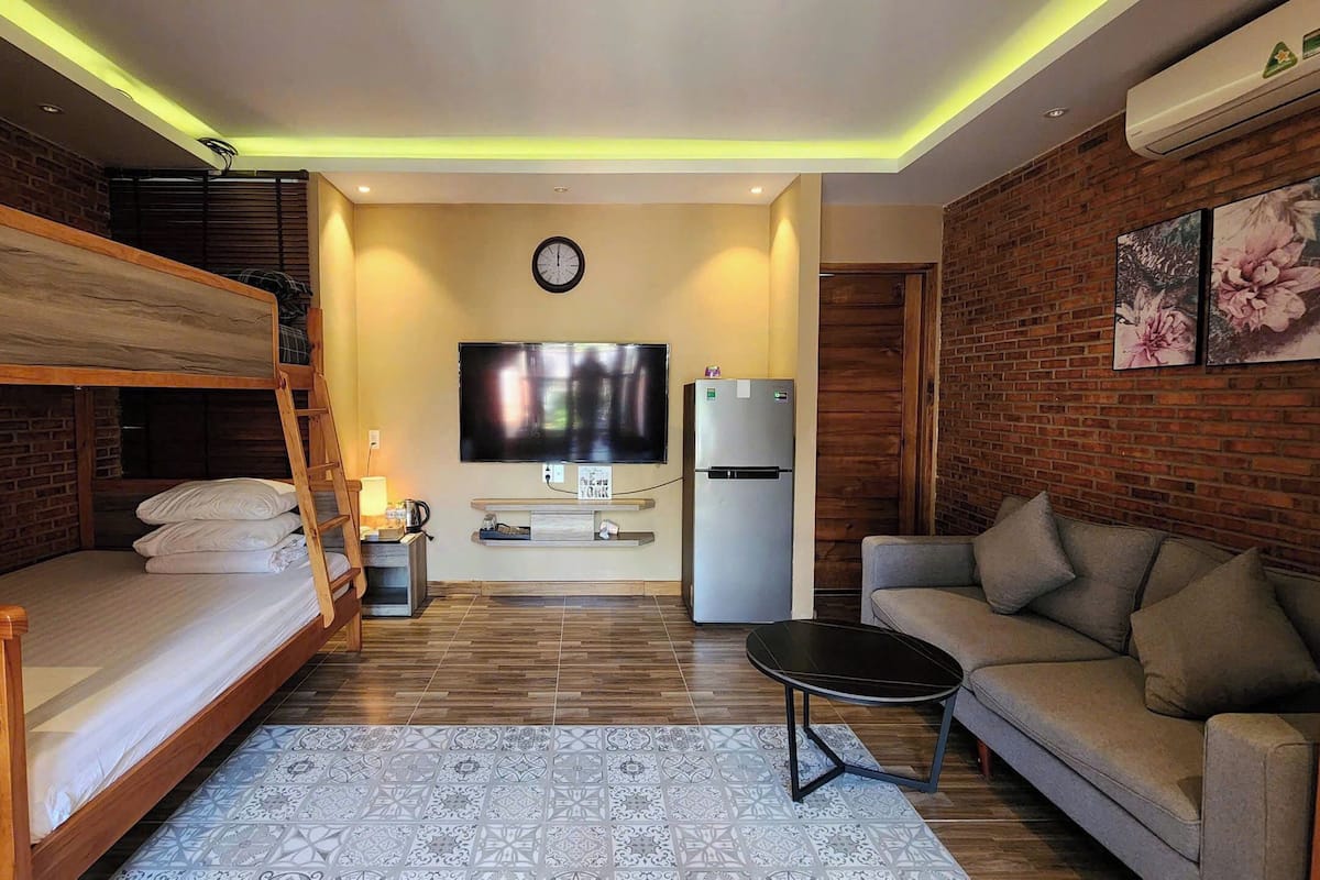 A compact living space with a bunk bed, a sofa, a TV, a refrigerator, and a patterned rug.
