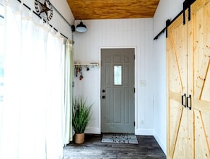 Una puerta de madera con un felpudo que dice 'Home', una planta en maceta y una lámpara fijada a la pared.