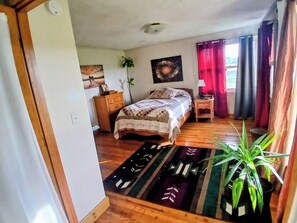 Una camera da letto con un letto, una cassettiera, un comodino, una pianta in vaso e un’opera d’arte appesa al muro.