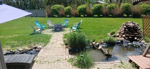 Un giardino con un braciere, un'area salotto esterna, un piccolo stagno e un patio in legno.