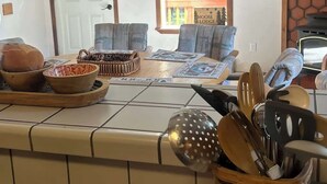 Keittiössä on liesi, ruokapöytä tuoleineen, ikkuna, josta avautuu näkymä puita kohti, ja kyltti, jossa lukee: ”Hirvimaja”.