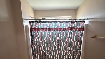 Un baño con cortina de ducha estampada, inodoro y alfombra verde.