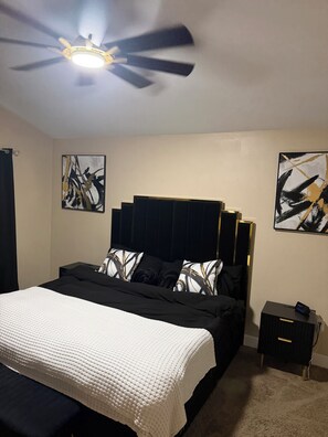Une chambre à coucher avec un lit, une table de chevet, un ventilateur de plafond et des œuvres d’art abstraites accrochées aux murs.