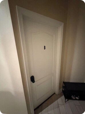 Una puerta blanca con un letrero 'B' negro, un pomo negro y un banco negro con zapatos.