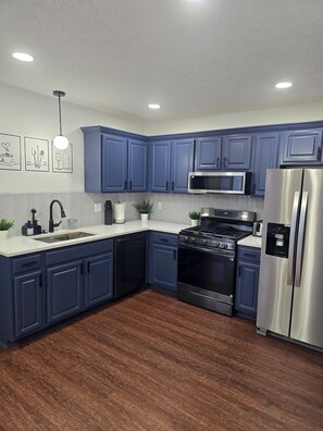 A modern kitchen with blue cabinets, a stainless steel refrigerator, a microwave, a stove, and a sink. - Family Legacy Retreat Downtown Indy 4BR Culture & Comfort (Indianapolis)