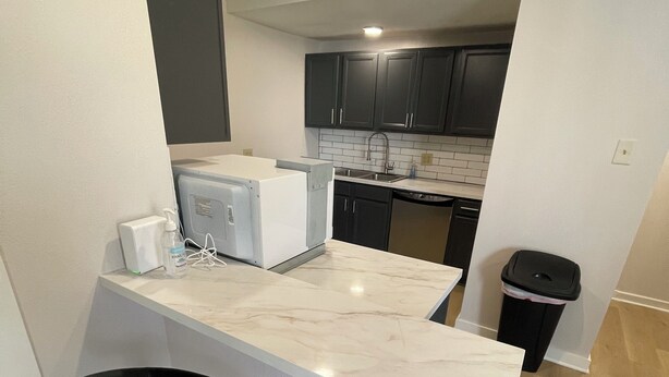Una cocina compacta con armarios oscuros, una encimera blanca y un taburete negro.