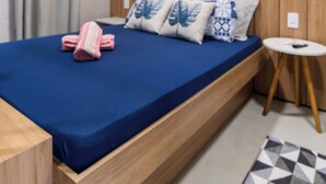 A modern bedroom with a wooden headboard, a blue bedspread, and a geometric-patterned rug. - Studio for Work and Relaxation | Pool + AC | Pet Friendly | Novo Hamburgo (Novo Hamburgo)