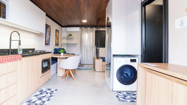 A compact kitchen with a washing machine, wooden cabinets, and a dining area with a chair. - Studio for Work and Relaxation | Pool + AC | Pet Friendly | Novo Hamburgo (Novo Hamburgo)