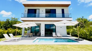 Una casa moderna de dos pisos con piscina, mobiliario exterior y un balcón.