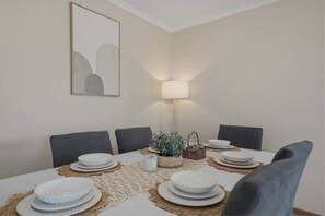 Un coin repas avec une table dressée pour quatre personnes, une lampe et une œuvre d’art encadrée accrochée au mur.