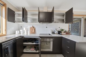 A compact kitchen with dark cabinets, a built-in oven, and a dishwasher. - Granton River Views Near Hobart Cozy Retreat (Granton)
