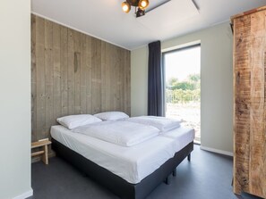 Ein Schlafzimmer mit einem Holz-Kopfteil, einem Bett mit weißer Bettwäsche, einer kleinen Holzbank und einem großen Fenster mit Blick.