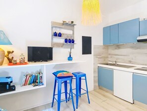 Una cocina moderna con armarios azules, encimera blanca y estufa integrada. Hay una pequeña zona de bar con taburetes y una estantería sobre el bar que alberga objetos decorativos.