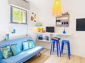 Una habitación con un sofá a rayas, un escritorio con una computadora, una lámpara y una lámpara colgante.