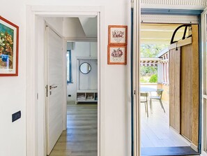 A hallway leading to a room with a wooden door, a round mirror, and framed pictures on the wall.