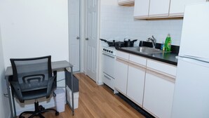 Una cucina compatta con pensili bianchi, un fornello, un lavello e una sedia.